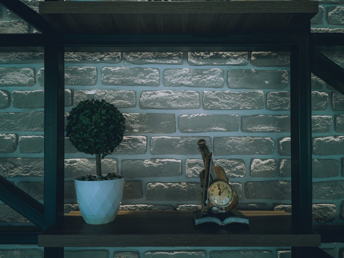 Chic shelf display featuring a violin-shaped clock and potted plant against a textured brick wall.
