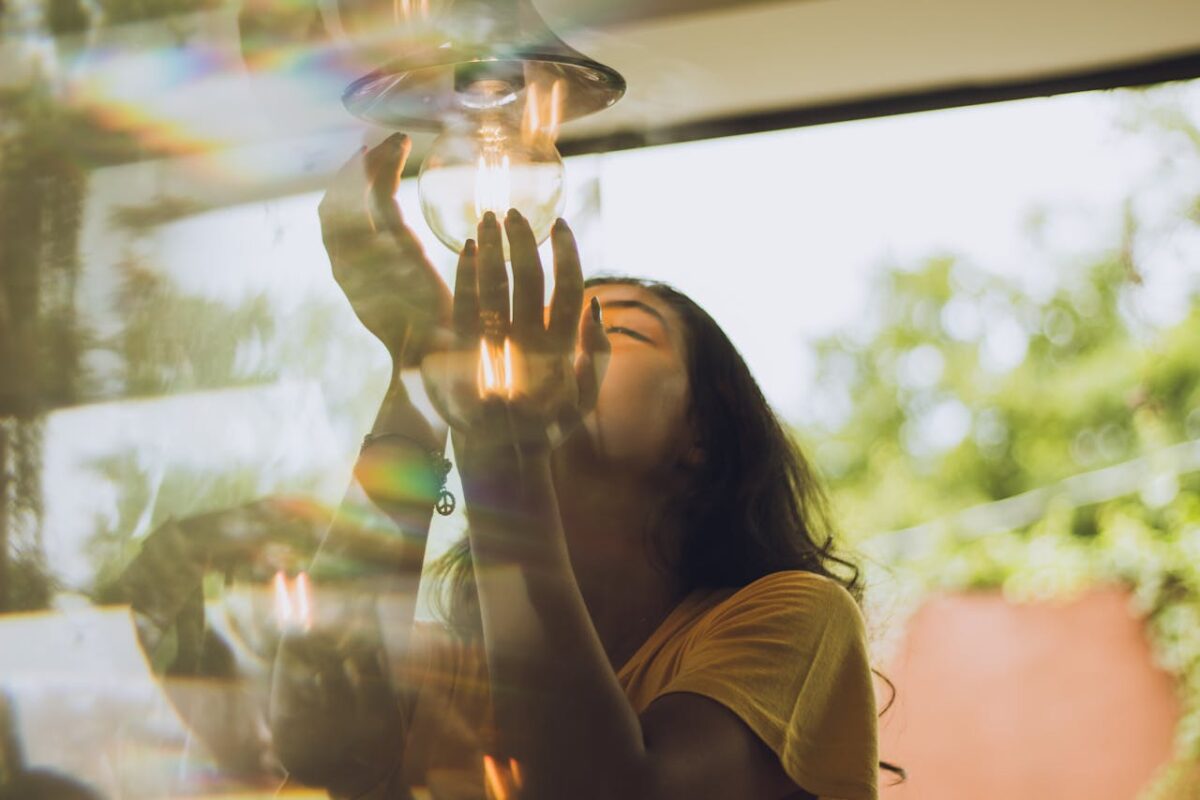 A woman holding a light bulb, capturing a prism light effect outdoors on a sunny day.