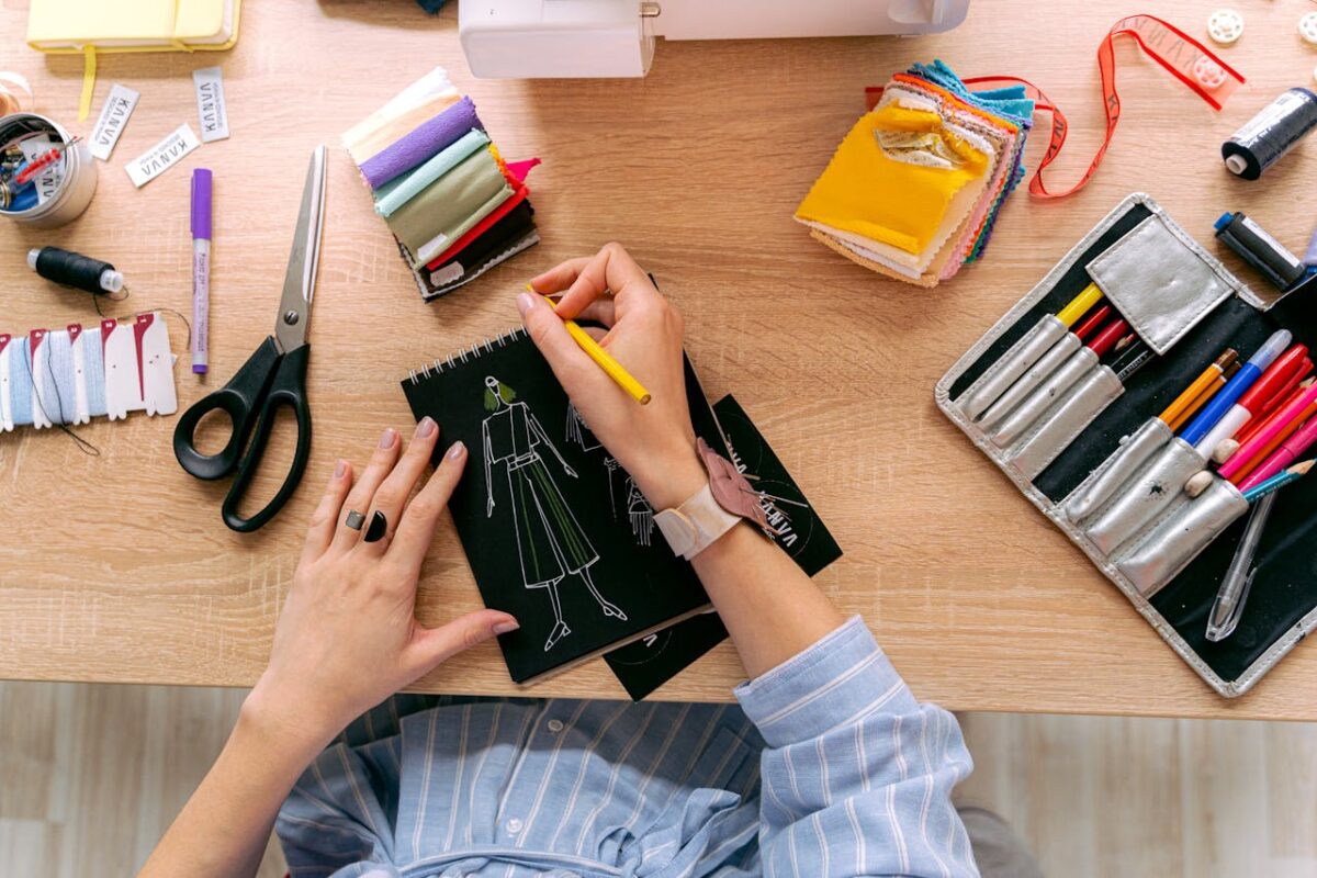 Designer sketching fashion outfits in a vibrant workshop with colorful fabrics and tools.